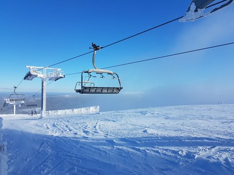 An empty ski lift going up a frozen and snowy mountain with blue sky above
