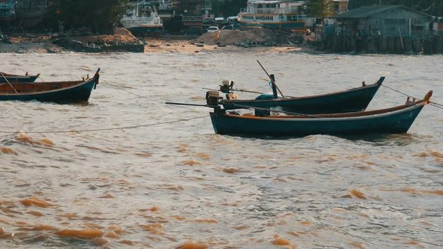 Small fishing boats sail along the lush sea on waves. Fishermen catch fish in the sea
