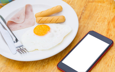 Close up the breakfast beside smartphone with blank space or white screen on the wooden table.