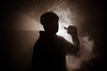 Vaping man holding a mod. A cloud of vapor. Black background. Vaping an electronic cigarette with a lot of smoke. Vape concept