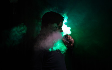 Vaping man holding a mod. A cloud of vapor. Black background. Vaping an electronic cigarette with a...