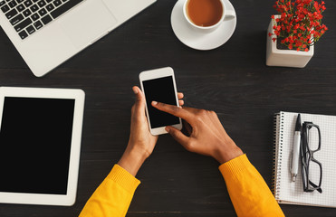 Black female hands holding smartphone, top view
