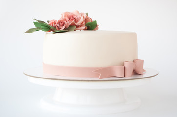 Art cake decorated with pink flowers and green leaves from mastic on a white background.