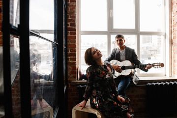 stylish adult couple having fun in cozy bedroom in style loft,  feeling happy being together. the man plays and sings on a guitar for the woman.