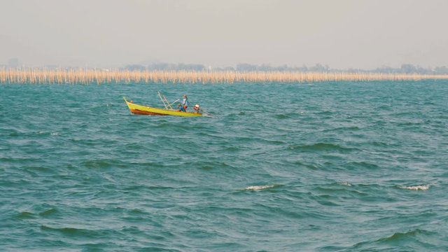 Yellow small fishing boat with people floating on a riotous blue sea, against the background of an oyster farm