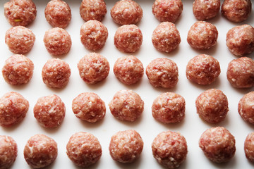 Freshly cooked raw meatballs lie on a white plastic board.