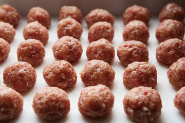 Freshly cooked raw meatballs lie on a white plastic board.