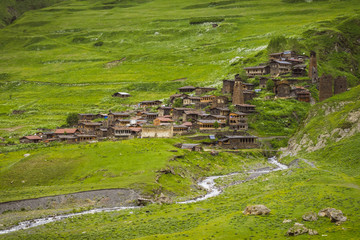Remote medieval Tushetian village with defencive towers (Dartlo, Georgia). Hills covered with green grass. Some huge stones could be seen on the foreground. The river runs down the hill.