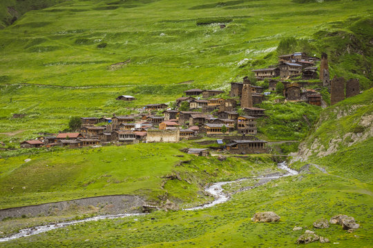 Remote medieval Tushetian village with defencive towers (Dartlo, Georgia). Hills covered with green grass. Some huge stones could be seen on the foreground. The river runs down the hill.