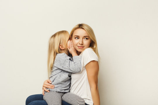 Little daughter whispering secret to her mother at white background - Powered by Adobe