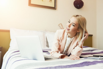 Happy businesswoman lying on bed and using tlaptop