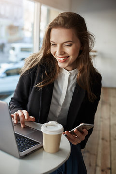 I need left positive feedback about this coffee shop. Portrait of charming stylish woman in cafe, browsing in net via laptop, holding smartphone and drinking tea, using free wifi and enjoy free time
