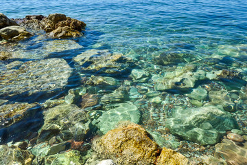 Transparent sea water seethes at the shore. Large coastal colored stones in the water. Beautiful abstract background.