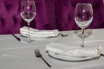 on the table with a white tablecloth is a cutlery for two that is made up of forks, knives, plates, glasses for wine, white napkins