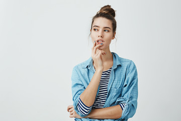 Girl making up plan what to do next. Portrait of thoughtful curious woman with bun hairstyle, holding fingers on lips while looking aside and thinking about something that bothers her