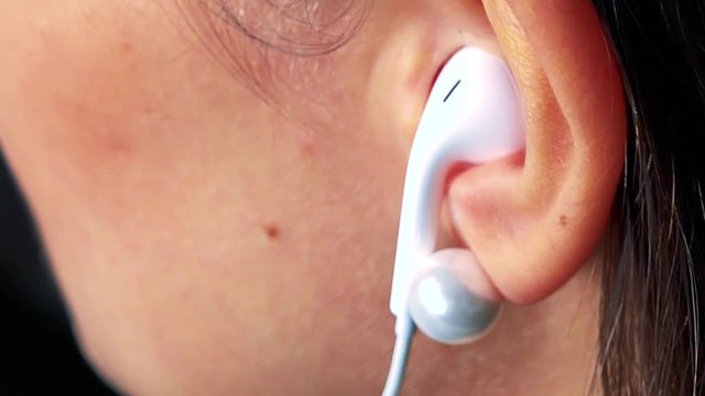 A woman puts earpieces in her ears and listens to music - ear closeup
