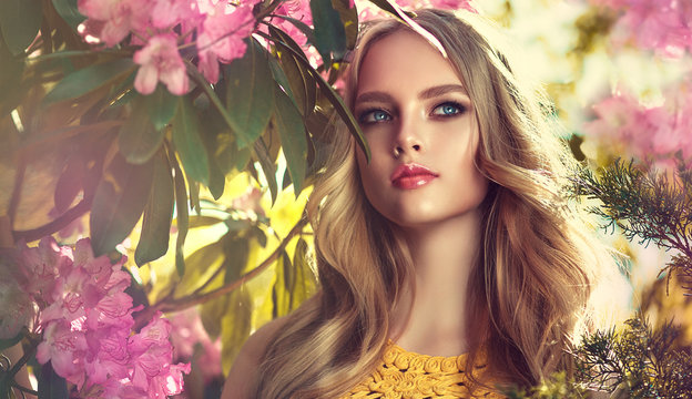 Beautiful spring   model girl   in flowers  in summer blossom park. Woman in a blooming garden . Fashion, Cosmetics & Perfumes . Curly blonde hair

