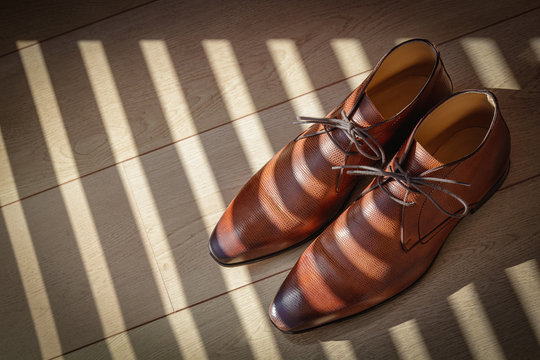 stylish brown leather men's shoes on a light wooden floor in a striped light pattern
