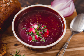 bowl of borscht with pieces of bread and onions on a wooden table