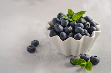 Ripe sweet blueberries in white bowl on a gray concrete background, selective focus, copy space.