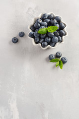 Ripe sweet blueberries in white bowl on a gray concrete background, top view, flat lay, copy space.