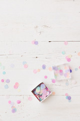Top view on small box full of colorful tissue paper confetti on white wooden table background.