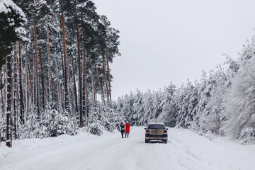 Girls in the middle of the road talking on the phone by car on a snowy road in a pine forest