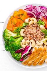 Buddha bowl dish with chicken fillet, brown rice, pepper, tomato, broccoli, onion, chickpea, fresh lettuce salad, cashew and walnuts. Healthy balanced eating. Top view. White background