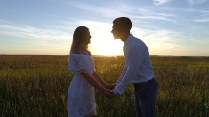 Fototapeta na wymiar Young beautiful couple in a wheat field. Silhouette on sunset background. Slow motion