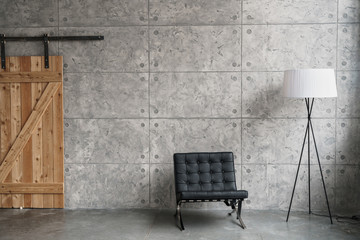 light loft design with gray paneled walls, black armchair, wooden doors on rollers and a lamp.