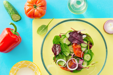 Healthy food background. Large bowl of fresh summer salad with ingredients for cooking salad on blue background, top view