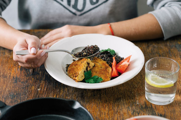 Healthy vegetarian food concept. Woman eating vegetarian food (black quinoa and cutlets from oatmeal and prunes) on wooden table