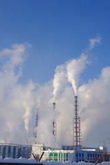 Factory, fenced by barbed wire, with many large chimneys producing clouds of white smoke