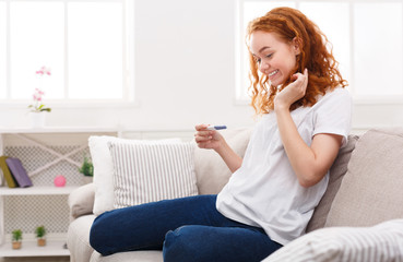 Happy girl with pregnancy test sitting on sofa
