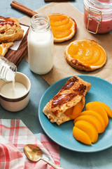 Milk is poured from the bottle into the cup. Fresh puffs with peach.