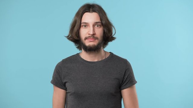 Portrait of emotional guy wearing casual gray t-shirt smiling and gesturing with hand meaning enough or can no longer, over blue background. Concept of emotions