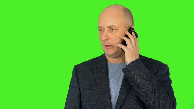 Bald caucasian man look to camera and hold smart phone at ear. Caucasian man talks by phone. Man speaking pn phone. Alpha channel, keyed green screen.
