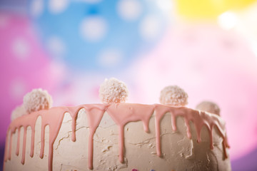 detail of a pink white birthday cake with coconut balls colorful balloon background