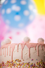 detail of a pink white birthday cake with coconut balls colorful balloon background