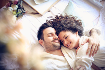 Happy young couple in bed . - obrazy, fototapety, plakaty