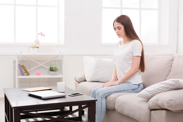 Pensive girl with gadgets on sofa