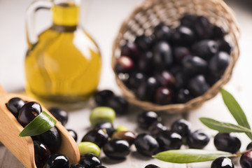 Olives and a bottle of olive oil on white dark wooden table