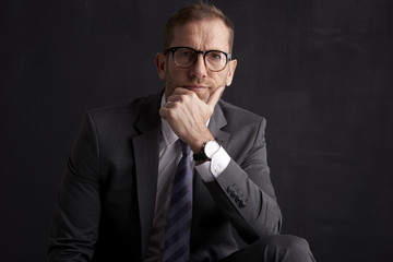 Thinking businessman portrait. Studio shot of wrinkled face business man wearing suit and looking thoughtful while sitting at dark background. Professional man wearing suit and tie. 