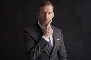 Thinking businessman portrait. Studio shot of wrinkled face business man wearing suit and looking thoughtful while sitting at dark background. Professional man wearing suit and tie. 