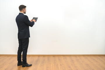 The businessman holding a tablet on the white wall background