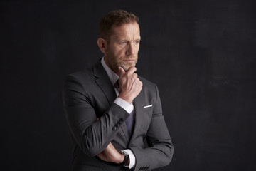 Nervous, overwhelmed businessman portrait.  Stressed businessman hand is on his forehead while sitting at dark background and thinking very hard. Professional man wearing suit.