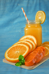 Slices of orange, mandarin and lemon and yellow juice in a glass on blue background