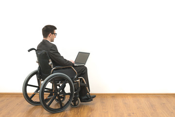The happy disabled in a wheelchair works with a laptop on a white wall background