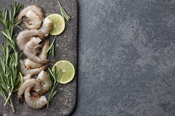 Foto auf Leinwand Cooking fresh raw tiger prawns with rosemary, lemon, lime, garlic and spices on stone countertop, top view © kobeza