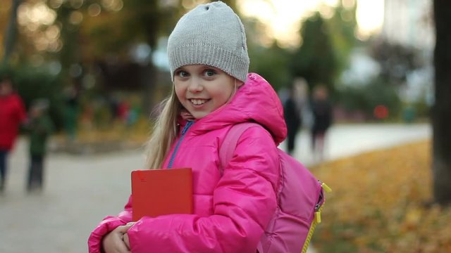 Pretty, blonde, school miss with school backpack, looking at camera in city. 